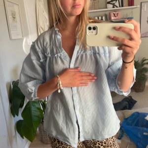 Blå- och vitrandig blus - Snygg blå- och vitrandig blus med v-ringning och knappar framtill. Blusen har trekvartsärmar och en lös passform, perfekt för en avslappnad stil.