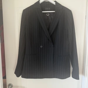 Svart randig kavaj från MQ - Snygg svart kavaj med vita ränder från MQ Dubbelknäppt design med klassisk krage och långa ärmar. Perfekt för en stilren look.