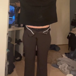 Bruna byxor med dragkedja - Snygga bruna byxor med en unik dragkedjedetalj framtill. Byxorna har en tight passform och är perfekta för en trendig look. De är högmidjade och ger en smickrande siluett.