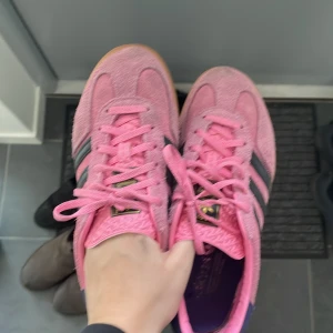 Rosa Adidas gazelle sneakers - Snygga rosa Adidas gazelle sneakers med svarta ränder och gummisula. Skorna har en klassisk design med snörning och är perfekta, dom e max använda 6 gånger❤️