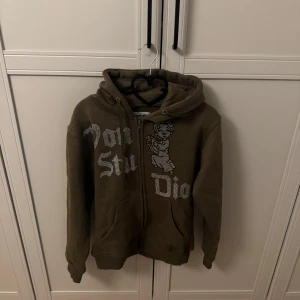 Von Studio Olivgrön hoodie - Säljer en olivgrön hoodie med dragkedja och tryck framtill. Den har en justerbar huva och långa ärmar. Perfekt för en avslappnad stil.Den är helt ny eftersom den inte passade mig.Pris kan diskuteras