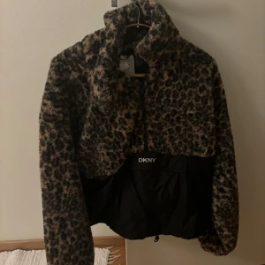 Leopardmönstrad teddyjacka från DKNY - Säljer en snygg leopardmönstrad teddyjacka från DKNY. Jackan har en dragkedja framtill och är perfekt för att hålla sig varm och trendig. Den har en croppad passform och är långärmad.
