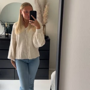 Beige stickad tröja med knappar - Säljer en mysig beige kofta med stora knappar framtill. Koftan har långa ärmar med ribbade muddar och en lös passform. 