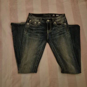 Blå jeans från Miss Me - Snygga blå jeans från Miss Me med dekorativa bakfickor och slitna detaljer. De har en lågmidjad passform och är perfekta för en avslappnad stil. Jeansen har en klassisk femficksdesign och knappar med logotyp. Jeansen är som helt nya knappt använda💕 skriv om ni har några frågor💕