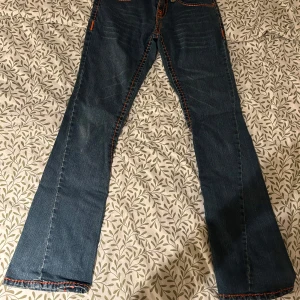 Blå jeans med färgglada sömmar från True Religion - Snygga blå jeans från True Religion med unika färgglada sömmar i orange och gult. De har en liten lagning i ena sidan som inte påverkar skicket💕 Annars är de i alldeles utmärkt skick🥰