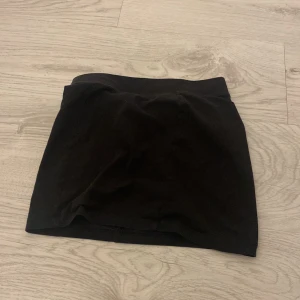 Svart kjol från H&M - Säljer en enkel och stilren svart kjol från H&M. Perfekt för en minimalistisk look. Kjolen är kort och har en elastisk midja för bekväm passform.