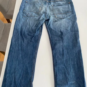 Blå jeansbyxor - Säljer ett par klassiska blå jeansbyxor med en straight passform. De har en dragkedja och knappar framtill samt fickor både fram och bak. Perfekta för en avslappnad stil.