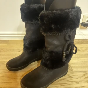 Svarta vinterstövlar med pälsdetaljer - Snygga svarta stövlar från Saint Galant  med mjuk pälsdetalj och dekorativa knytband med pärlor. Perfekta för kalla vinterdagar med en robust sula för bra grepp.