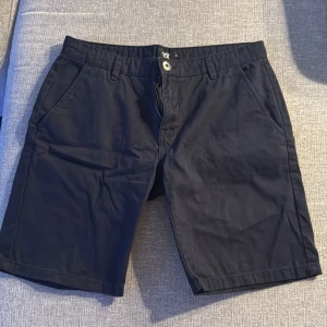 Svarta shorts med knappar - Snygga svarta shorts med knappstängning och dragkedja. De har två sidofickor fram och två bakfickor med knappar. Perfekta för en avslappnad stil.