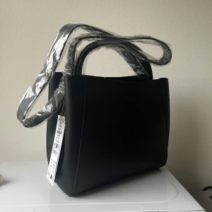 Gina tricot väska  - Svart väska från Gina Tricot. Modellen heter ”pu midi bag”, slutsåld online. Ca 27x22 cm. Helt ny med prislappen kvar! 