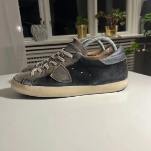Grå svarta philippe model sneakers med snörning - Snygga grå sneakers i mocka med snörning och en vit sula. Skorna har en stilren design med diskreta detaljer och en bekväm passform. Perfekta för en avslappnad stil. Skorna är ganska andvända men funkar bra fortfarande, har fräschats upp.
