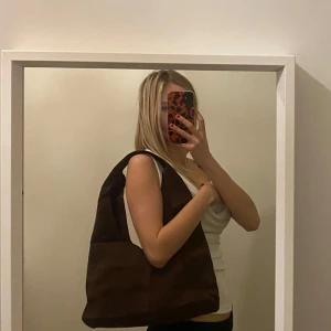 Brun axelväska i mocka - Snygg brun axelväska i mjukt mockamaterial. Perfekt för att bära med sig det nödvändigaste med stil. Enkel design som passar till många olika outfits.