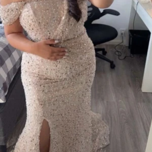 Champagnefärgad glittrig klänning - Säljer en elegant champagnefärgad klänning med glittrande paljetter. Klänningen är axelbandslös och har en lång design med en slits framtill. Perfekt för en glamorös kväll!