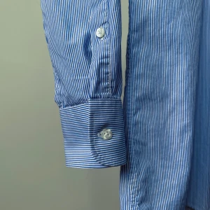 Vintags Barneys NY Cotton Blue Shirt - Barneys New York Striped Cotton Shirt with 7 White Buttons. Blue Mini Stripe. 1 Left Front Pocket. Best Worn Oversized. Model is 160cm (5”3) and generally fits S/M.  Minor tear in bottom left fabric. Small imperfections are not attributed to a design flaw but to the uniqueness and quality of the product, please appreciate them for their character. Overall Good Condition.  76 CM/ 29.9 IN Length 60 CM/ 23.6 IN Sleeve 46 CM/ 18.1 IN Shoulders 110 CM/ 43.3 IN Chest 104 CM/ 40.9 IN Waist