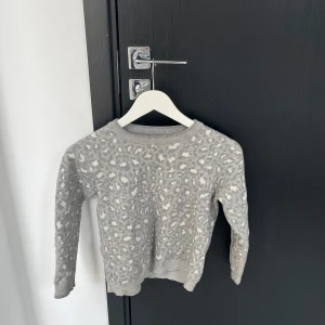 Grå leopardmönstrad stickad tröja - Säljer en mysig grå stickad tröja med leopardmönster. Tröjan har långa ärmar och en rund halsringning. Perfekt för kyliga dagar.