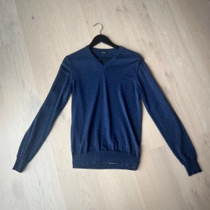Mörkblå tröja från J.Lindeberg - Säljer en stilren mörkblå tröja från J.Lindeberg. Tröjan har en v-ringad hals och långa ärmar, perfekt för en elegant look. Tillverkad i ett mjukt material som ger en bekväm passform. Passar utmärkt till både vardag och mer uppklädda tillfällen.