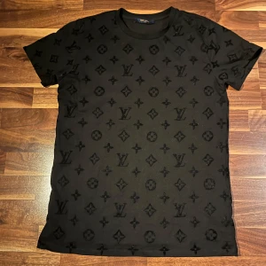 Svart t-shirt från Louis Vuitton - Snygg svart t-shirt från Louis Vuitton med det ikoniska monogrammönstret. Tillverkad i 100% bomull för en bekväm passform. Perfekt för dig som vill ha en stilren look med en touch av lyx. den är också värd 6000kr