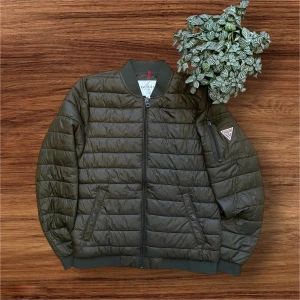 Olivgrön pufferjacka från Guess - Säljer en snygg khakifärgad tun pufferjacka från Guess. Jackan är använd max 10 gånger. Den är quiltad och har ribbade muddar vid ärmslut och nederkant. Perfekt nu när det börjar bli lite varmare och man inte vill ha sin tjocka dunjacka! Jag kan inte hitta exakt denna modell på internet men jag hittar en liknade där nypris är ungefär 2400kr och mitt pris är endast 299kr. Jag rekommenderar jackan starkt. Hör gärna av dig om du har några frågor!