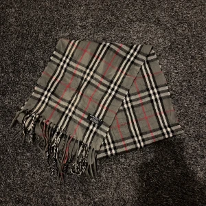 Rutig halsduk från Burberry - Snygg rutig halsduk från Burberry i klassiska färger. Tillverkad i 100% kashmir för en lyxig och mjuk känsla. Perfekt accessoar för att hålla dig varm och stilren under kyliga dagar.