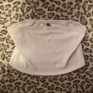 Vit ribbad tubtopp  - Säljer en stilren vit tubtopp. Toppen är axelbandslös och har en tight passform som framhäver figuren. 