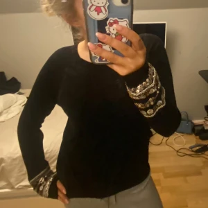 Svart unik tröja - Säljer en svart tröja med långa ärmar och vackra broderade detaljer i silver och guld på ärmsluten. 