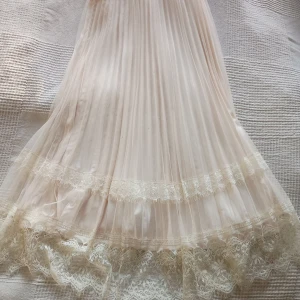 Champagnefärgad kjol med spetsdetaljer och glitter. - Elegant champagnefärgad kjol  med vackra spetsdetaljer och ett skirt, glansigt material. Ubderkjole. Har holografiskt glitter som skimmrar igenom  Perfekt för speciella tillfällen med sin romantiska och dömlika stil.