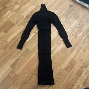 Svart ribbad långklänning - Snygg svart ribbad långklänning med polokrage och långa ärmar. Perfekt för en stilren look. Klänningen har en tight passform som framhäver figuren.