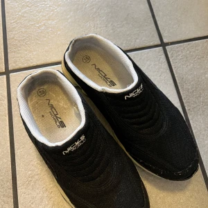 Svarta sneakers från Nick's World - Snygga svarta sneakers från Nick's World med vit sula och bekväm passform. Skorna har en stilren design med textilmaterial och en robust yttersula för bra grepp. Perfekta för en avslappnad stil.