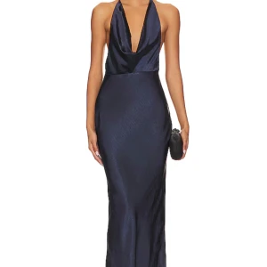 Mörkblå långklänning från Runaway The Label - Elegant mörkblå långklänning från Runaway The Label med öppen rygg och halterneck-design. Klänningen har en vacker drapering framtill och är tillverkad i ett glansigt material som ger en lyxig känsla. Perfekt för speciella tillfällen. Bara testad 🦋