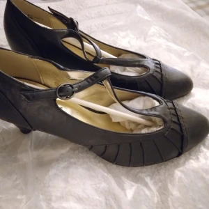 HELT NYA, OANVÄNDA Svarta Pumps i Retro / vintage -stil, Graceland, 36 - Eleganta svarta pumps från Graceland. Dessa skor har en klassisk, lite retro/vintage design som påminner lite om dans-skor, med en smickrande rem över foten. Perfekt för både vardag och festligare tillfällen. Bekväma och stilrena. Storlek: 36. Helt nya och oanvända. Skickas i orginalbox/tillhörande skokartong.