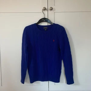 Blå stickad tröja från Polo Ralph Lauren - Snygg blå stickad tröja från Polo Ralph Lauren med kabelstickat mönster och röd broderad logga på bröstet. Skriv till mig om ni är intresserade👍pris kan diskuteras 