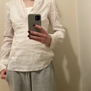 Vitt blus  - En snygg vit blus som ger en klassisk look. Tyget har render med glansigare vitt färg. Väl använd men i väldigt bra skick.