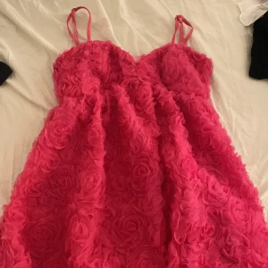 Rosa klänning med rosdetaljer - Kort jätte gullig rosa klänning med vackra rosdetaljer över hela tyget. Klänningen har smala axelband och en dragkedja i ryggen för enkel påklädning. Perfekt för en romantisk look. Eller gullig somrig look💕 pris kan diskuteras, klänningen är använd en gång på midsommar så inga defekter 