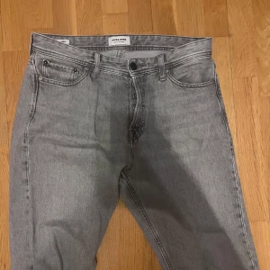 Grå jeans från Jack & Jones - Snygga grå jeans från Jack & Jones. De har en knappgylf och är perfekta för en avslappnad stil. Passformen är normal och de är tillverkade i ett slitstarkt jeanstyg.