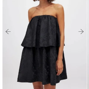 Svart axelbandslös klänning - Snygg svart axelbandslös klänning med volangdetaljer från NAKD. Den är alrig använd med prislapp kvar. Nypris ligger på 599kr!