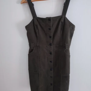 Olivgrön klänning med knappar - Snygg olivgrön klänning med knappar framtill och justerbara axelband. 