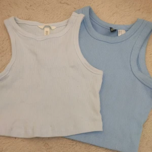 Två ribbade linnetoppar från H&M - Säljer två snygga ribbade linnetoppar från H&M i ljusblå och blå nyans. Perfekta för en avslappnad stil. Topparna är ärmlösa och har en bekväm passform. Storlek XS knappt använd.