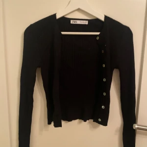 Svart kofta från Zara - Snygg svart kofta från Zara med knappar framtill. Perfekt för lager-på-lager och att hålla sig varm under kyligare dagar. Koftan har en ribbad struktur som ger en stilren look.