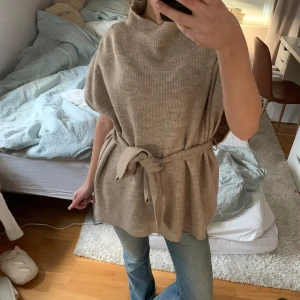 Beige ribbad tröja med bälte - Säljer en snygg beige ribbad tröja med bälte i midjan. Tröjan har en lös passform och korta ärmar.