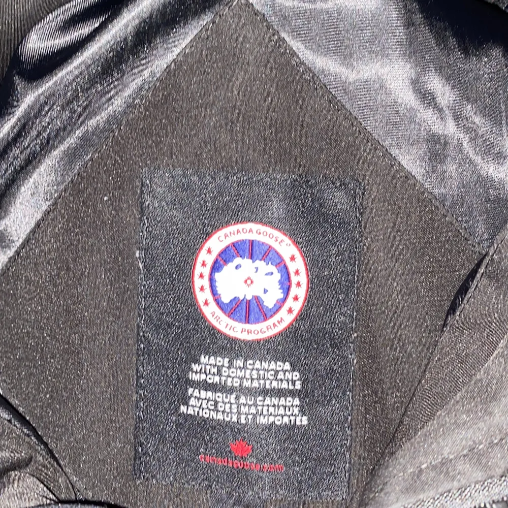 Säljer en svart dunjacka från Canada Goose med en avtagbar huva och pälsdetaljer. Jackan har en broderad logotyp på ärmen och stängs med dragkedja och knappar. Perfekt för kalla vinterdagar.. Takit.