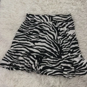 Zebramönstrad kortkjol - Snygg zebramönstrad kortkjol med volangdetaljer. Perfekt för att sticka ut med en djärv look. Kjolen har en bekväm passform och är lätt att matcha med olika toppar.