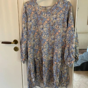 Blommig klänning från Soyaconcept - Charmig blommig klänning från Soyaconcept i ljusblått och beige. Klänningen har långa ärmar och ett vackert mönster med blommor. Perfekt för en avslappnad och stilfull look.