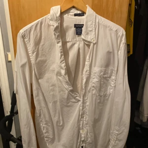 Vit skjorta från GANT(storlek s/m) - Klassisk vit skjorta från GANT med lång ärm och knappar framtill. Perfekt för en stilren look. Skjortan har en bröstficka och en krage som ger en tidlös stil.