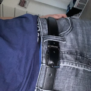 Calvin Klein svart skärp i skinn - Snyggt svart skärp i skinn med en stilren design. Perfekt för att ge en klassisk touch till din outfit. Skärpet har ett silverfärgat spänne som ger en elegant kontrast.