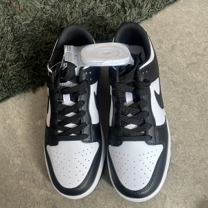 Nike Dunk i svart och vitt - Snygga Nike Dunk sneakers i klassisk svart och vit färgkombination. Skorna har en stilren design med svart snörning och en vit sula. Perfekta för en sportig och trendig look. Den passade inte mig, därför vill jag sälja den för samma pris eller någorlunda billigare . Bud funkar bra!!
