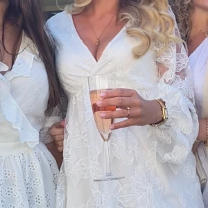 Vit studentklänning med blommigt mönster - Säljer en vacker vit klänning med blommigt mönster och v-ringning. Klänningen har långa ärmar och en luftig passform, perfekt som studentklänning. Inte använd på studentflaket!!! 