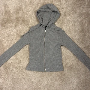 Grå ribbad hoodie från Gina Tricot - Säljer en stilren grå ribbad hoodie från Gina Tricot. Den har en dragkedja framtill och en bekväm huva. Säljer pågrund av att den aldrig användes. 
