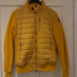 fleece och pufferjacka från Parajumpers - Säljer en gul fleece och pufferjacka från Parajumpers. Jackan har en quiltad design med dragkedja framtill och flera praktiska fickor. Perfekt för vår dagar med sin kombination av fleece och puffer för extra värme. Finns en liten fläck som knappt syns (en av bilderna)