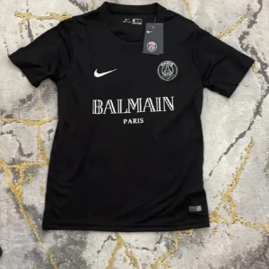 Svart PSG x Balmain fotbollströja - Snygg svart PSG x Balmain fotbollströja från Nike. Tröjan har korta ärmar och ett stilrent tryck med Balmain Paris-logga på bröstet. Perfekt för fotbollsfans som vill ha något unikt och trendigt.