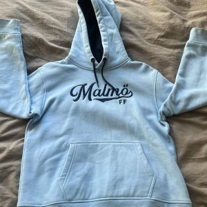 Ljusblå hoodie från Malmö FF - Säljer en ljusblå hoodie från Malmö FF med mörkblå text på framsidan. Tröjan har en stor ficka framtill och en justerbar huva med mörkblåa snören. Perfekt för alla Malmö FF-fans!🩵Lite stänk fläckar 